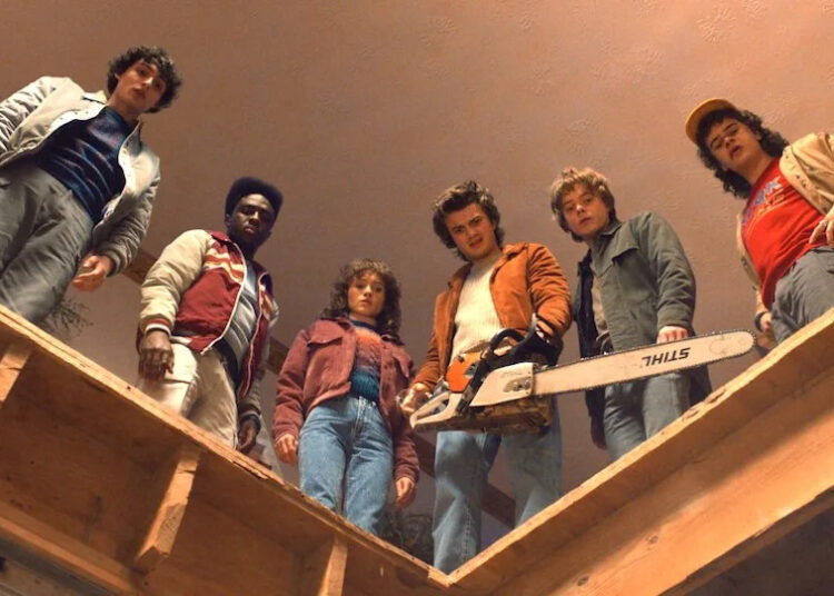 The cast of Stranger Things 5 looks down from high aboce on wooden beams as Steve holds a chainsaw