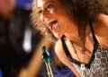 Smiling widely, Vanessa Collier leans over her saxophone.