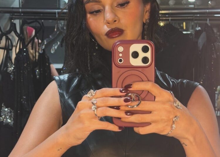 a person taking a selfie while dressed in a black leather outfit with accessories visible