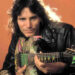 Steve Vai posing for a photograph while holding a guitar in 1990.
