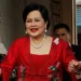Reuters Queen Sirikit, wearing pearl jewellery and a red dress, is helped down a staircase by guards in uniform.