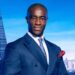 Tim Campbell posing for The Apprentice 2024. He is wearing a blue suit and is in front of a background of the London skyline