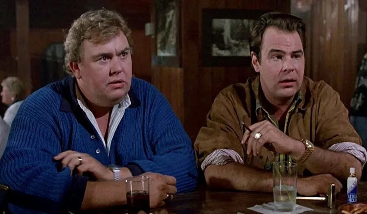John Candy's Chet Ripley sitting at a bar next to Dan Aykroyd's Roman Craig in The Great Outdoors