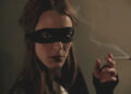 A masked woman smoking a cigarette in 50 Kisses