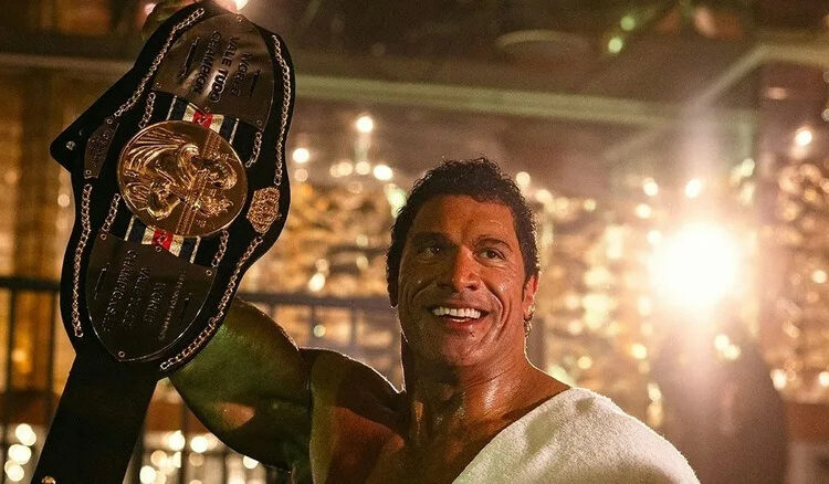 Dwayne Johnson as Mark Kerr holding up a championship belt in The Smashing Machine