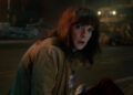 Winona Ryder as Joyce Byers crouched in the street with a look of horror on her face in Stranger Things