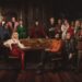 The cast of The Celebrity Traitors stand around a circular table wearing poker faces whilst the show's host, Claudia Winkleman, stands centre.