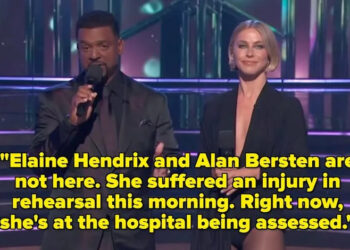 Two hosts on a stage with performers in the background. The male host wears a dark suit, and the female host is in a sleek, form-fitting outfit