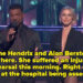 Two hosts on a stage with performers in the background. The male host wears a dark suit, and the female host is in a sleek, form-fitting outfit