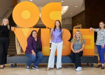 Five Titan alumni who work for the OCVIBE development pose in front of a display.
