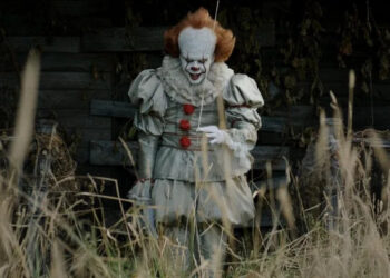 Pennywise standing in front of a dilapidated building in It