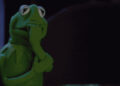 Kermit the Frog, looking nervous, bites his hand in a dramatic moment from a TV show or movie scene
