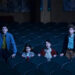 Four children stand among empty theater seats, looking intently ahead, suggesting a scene from a movie or show