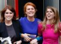 Princess Beatrice, Sarah Ferguson and Princess Eugenie in dresses smile as they link arms walking