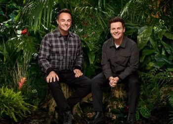two individuals seated on a log amidst dense tropical foliage