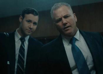 Sean Carrigan as John Douglas and Caleb Ruminer as Robert Ressler looking through a one-way mirror on Monster: The Ed Gein Story