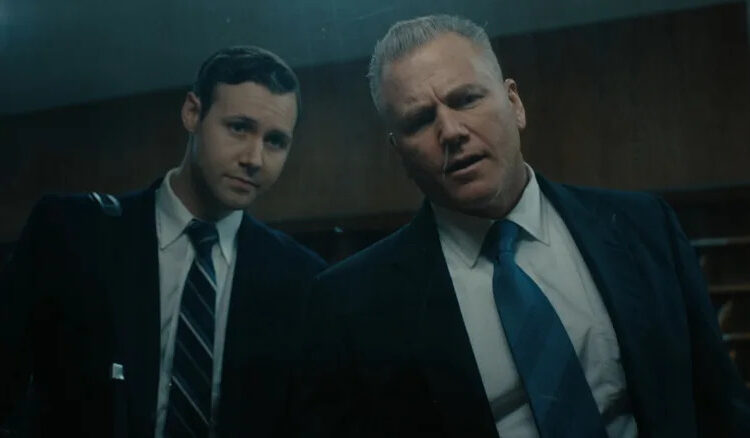 Sean Carrigan as John Douglas and Caleb Ruminer as Robert Ressler looking through a one-way mirror on Monster: The Ed Gein Story