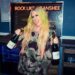 Person in a camo hoodie holding two wine bottles, tongue out, with "Rock Like a Banshee" sign.