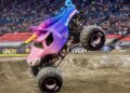 a monster truck decorated as a pink and purple unicorn in a dirt arena