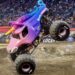 a monster truck decorated as a pink and purple unicorn in a dirt arena