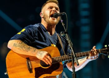 Country artist Zach Bryan singing onstage with intensity, reflecting the bold spirit of his track “Bad News” that challenges law enforcement and sparks debate.
