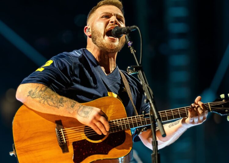 Country artist Zach Bryan singing onstage with intensity, reflecting the bold spirit of his track “Bad News” that challenges law enforcement and sparks debate.