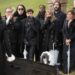 A group of funeral mourners gasp in front of an open coffin