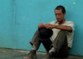 Roy Scheider as Jackie Scanlon in Sorcerer, looking really dirty and sitting against a blue wall.