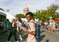 A man holding a book walking in front of the Texas Capitol building