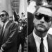 Two black-and-white photos of a man in a suit and dark sunglasses. In the left photo, he is being interviewed on courthouse steps; in the right, he is seen close up, looking thoughtful among a crowd.