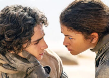 Two actors in a dramatic scene from a sci-fi film; one holds the other's face as they exchange an intense gaze