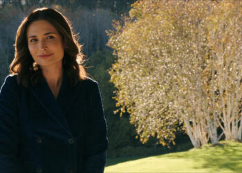Zosia smiling slightly standing in front of a tree on Pluribus