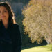 Zosia smiling slightly standing in front of a tree on Pluribus