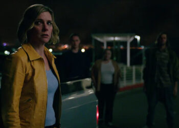 Rhea Seehorn as Carol Sturka looking worried beside a pickup truck with shadowy people in the background in Pluribus