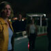 Rhea Seehorn as Carol Sturka looking worried beside a pickup truck with shadowy people in the background in Pluribus