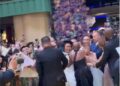 Fans line up behind a barrier. On a bright yellow carpet, security move toward women in gowns to remove a man in a tshirt, who put his arm around one of the women.