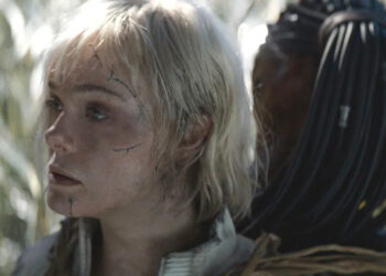 Elle Fanning as Thia looking to the side while attached to Dek in Predator: Badlands .