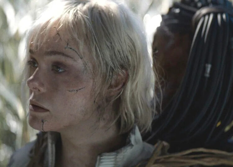 Elle Fanning as Thia looking to the side while attached to Dek in Predator: Badlands .
