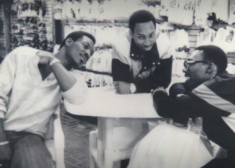 A black and white image of three men leaning on a table.