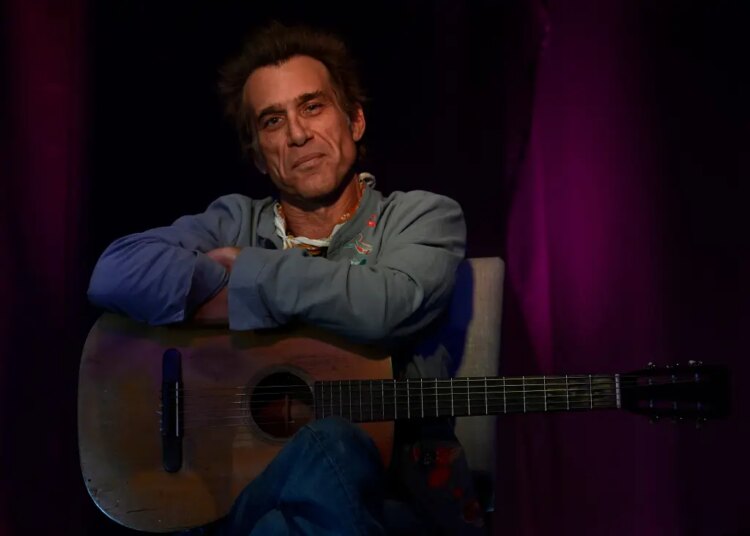 Todd Snider sitting with an acoustic guitar.