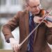 A white man wearing glasses and a brown sport coat plays a violin. Andy Carlson directs the Greenvillebillies, Bluegrass Ensemble concert