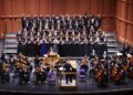 An orchestra and choral group on risers on a stage perform Handel's Messiah