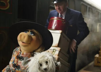 Miss Piggy carrying her dog while her butler carries her bags through a train station in Muppets Most Wanted