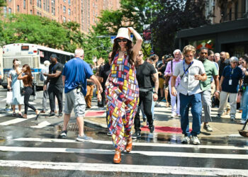 Hathaway holds on to her hat as she walks across a street.