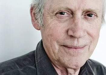 Archie Fisher is looking into the camera and half smiling. He has grey hair but the photo has been cropped at his forehead. He is wearing a grey shirt.