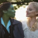 Cynthia Erivo's Elphaba and Ariana Grande's Glinda looking at each other smiling on the set of Wicked: For Good with poppy fields behind them.