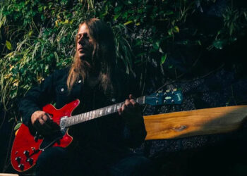 Sammy Boller is photographed in front of some foliage with a red Gibson ES-335.