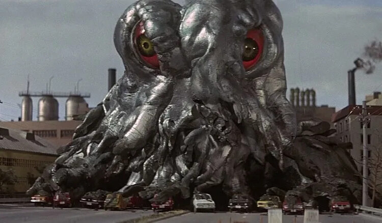 Hedorah eating up some cars outside a factory in Godzilla vs. Hedorah