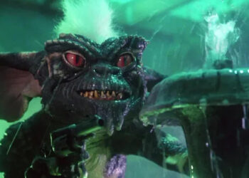 Stripe holding a gun with murderous intent and standing behind a fountain in Gremlins