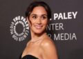 Meghan Markle posing elegantly on the red carpet in a designer gown, smiling for photographers.